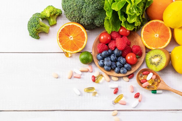 Top view of fresh fruits and vegetables with different medicine on a wooden spoon