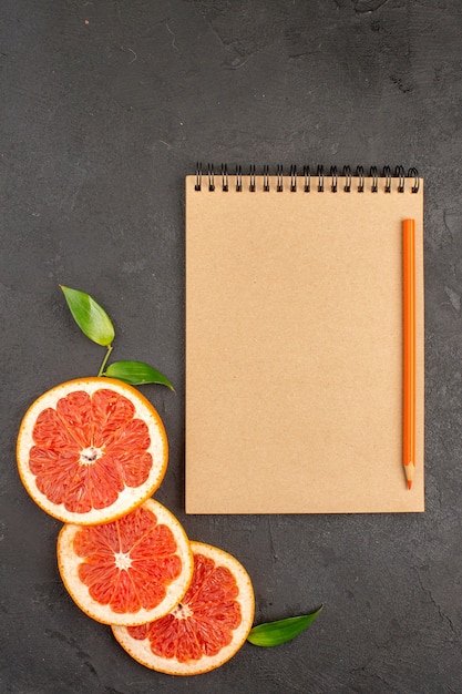 Free photo top view fresh grapefruit slices with notepad on a dark background