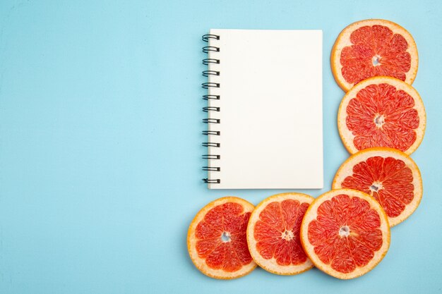 Top view fresh grapefruits fruit slices with notepad on blue background