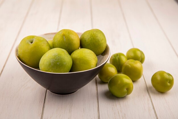 Top view of fresh green cherry plums on a black bowl with green cherry plums isolated on a wooden background