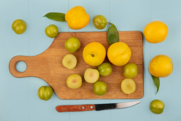 Vista dall'alto di prugne ciliegie verdi fresche su una tavola di cucina in legno con pesche gialle fresche su sfondo blu