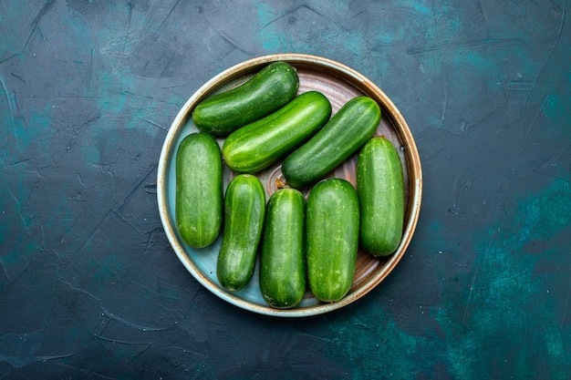 Top view fresh green cucumbers ripe vegetables inside plate on dark-blue desk.