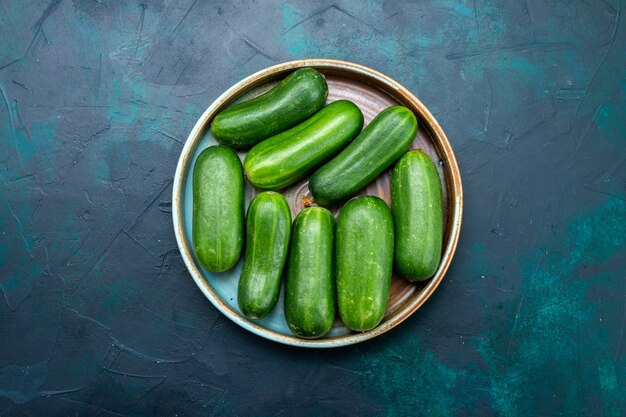 Top view fresh green cucumbers ripe vegetables inside plate on dark-blue desk.