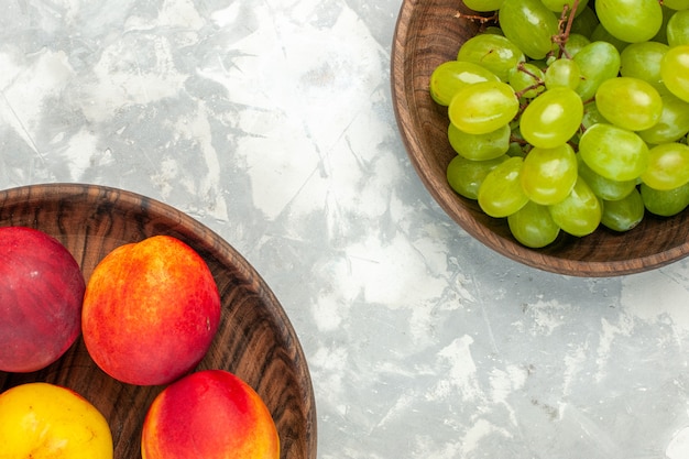 Вид сверху свежий зеленый виноград, мягкий и вкусный с персиками на светло-белом столе