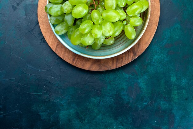 Top view fresh green grapes mellow and juicy fruits inside plate on the dark blue desk.