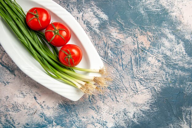 Top view fresh green onion with tomatoes on light-blue background