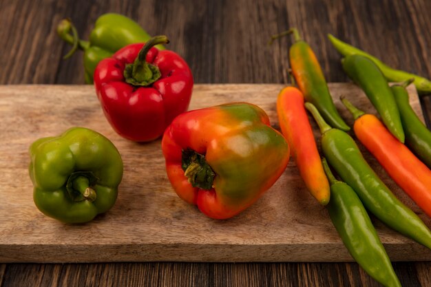 Top view of fresh green and orange peppers isolated on a wooden kitchen board on a wooden surface