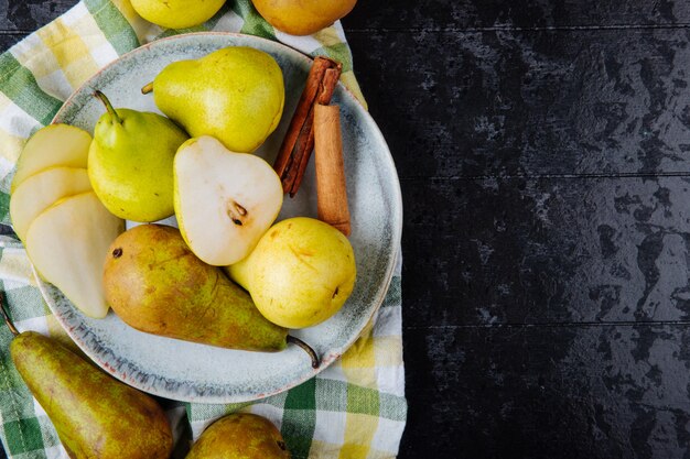 Top view of fresh green pears and pear halves on a plate on the plaid tablecloth on black background with copy space