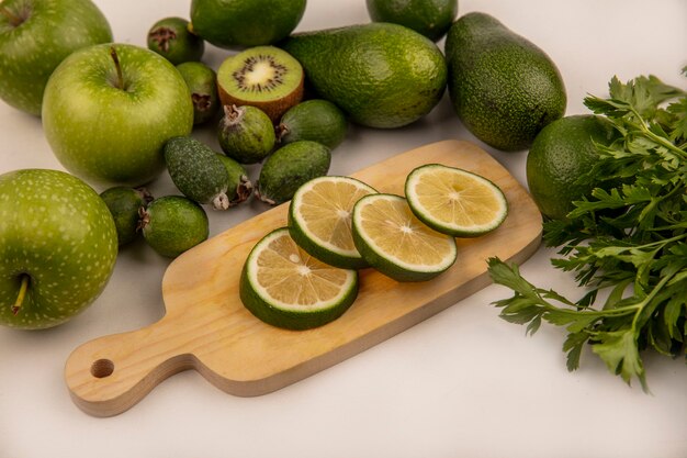 Top view of fresh green slices of limes on a wooden kitchen board with green apples kiwi and avocados isolated on a white background