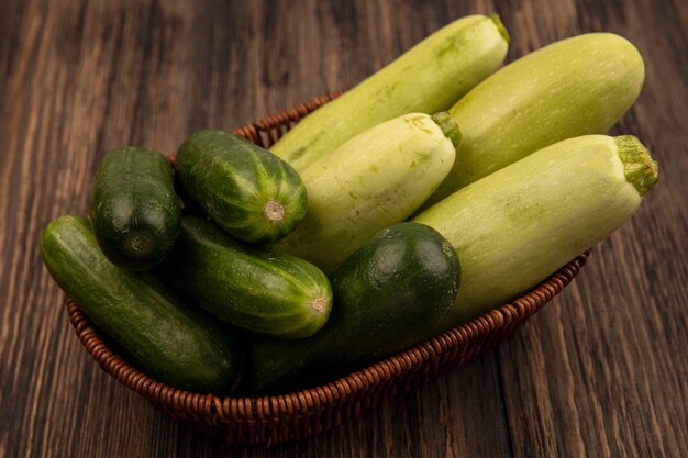 Top view of fresh green vegetables such as zucchinis and cucumbers on a bucket on a wooden surface