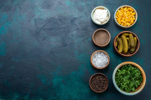 Top view fresh greens with pickles corns and seasonings on dark-blue desk.