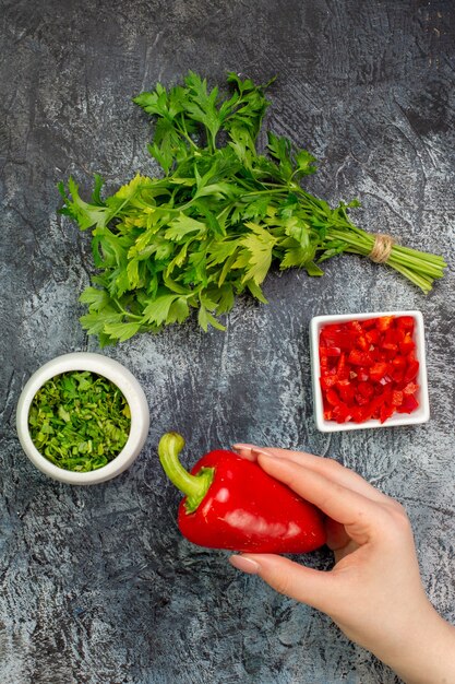 Top view fresh greens with red bell-peppers on a light-grey table