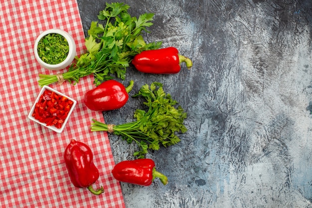 Top view fresh greens with red bell-peppers on light-grey table