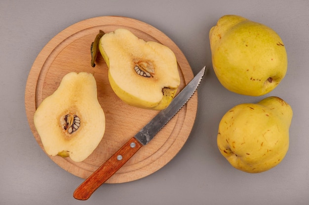 Top view of fresh halved quinces on a wooden kitchen board with knife with whole quinces isolated