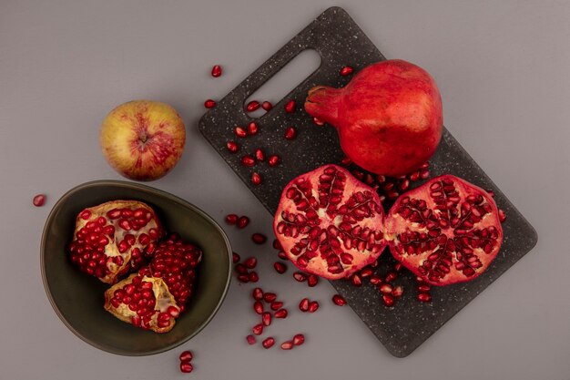 Top view of fresh halved and whole pomegranates on a black kitchen board with open pomegranates on a bowl