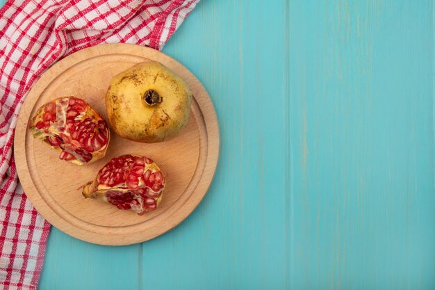 Top view of fresh halved and whole pomegranates on a wooden kitchen board on a checked cloth on a blue wooden wall with copy space