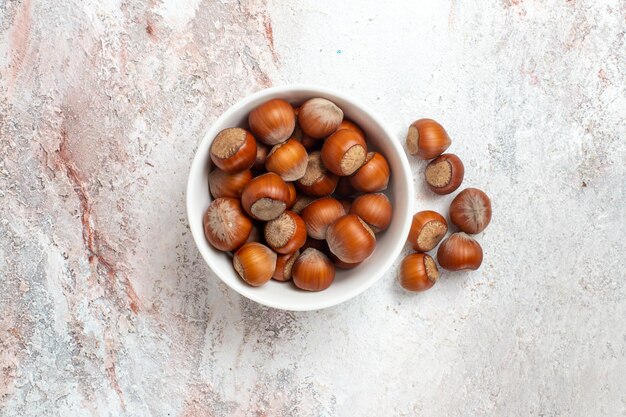 Top view of fresh hazelnuts inside plate on white surface