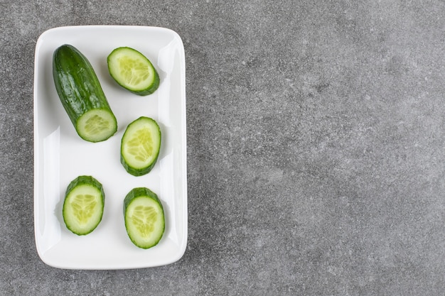 Top view of fresh healthy cucumbers n white plate over grey table.