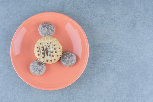 Top view of fresh homemade cookies. Delicious snacks on orange plate.