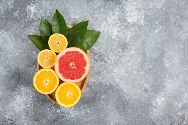 Top view of fresh juicy fruit slices with leaves on wooden plate.