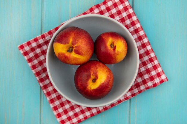 Top view of fresh juicy peaches on a bowl on a red checked cloth on a blue wooden wall