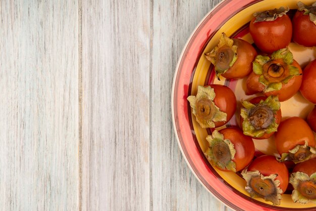 Free photo top view of fresh juicy persimmons on a plate on a grey wooden wall with copy space