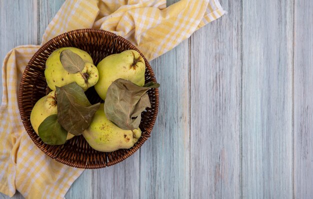 Top view of fresh juicy quinces with leaves on a bucket on a yellow checked cloth on a grey background with copy space
