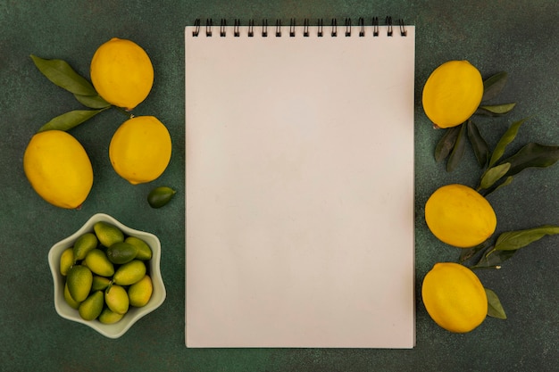 Top view of fresh kinkans on a bowl with lemons isolated on a green surface with copy space