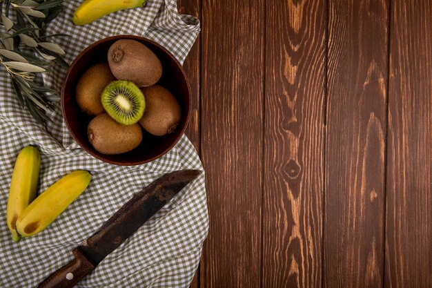 Top view of fresh kiwi fruit in a wooden bowl and fresh bananas with old kitchen knife on rustic with copy space