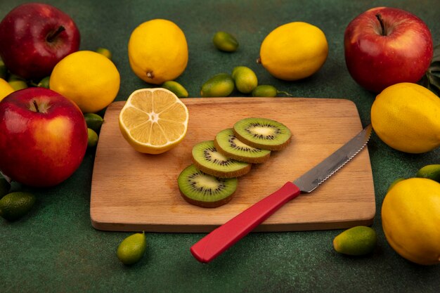 緑の表面に分離されたレモンとカラフルなリンゴとナイフで木製のキッチンボード上の新鮮なキウイスライスの上面図