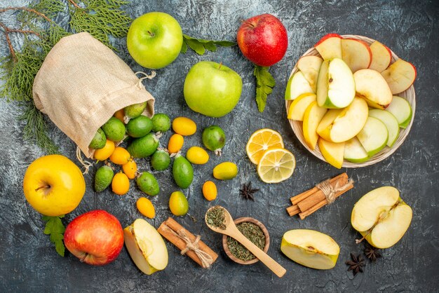 Top view of fresh kumquats inside and outside of a fallen small white bag and red yellow green apples fir branches on gray table