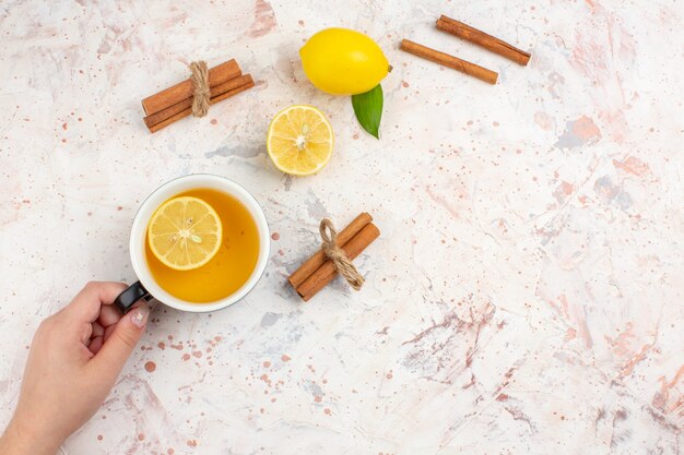 Вид сверху нарезанный лимоном лимонные палочки корицы чашка чая с лимоном в женской руке на яркой изолированной поверхности, свободное пространство