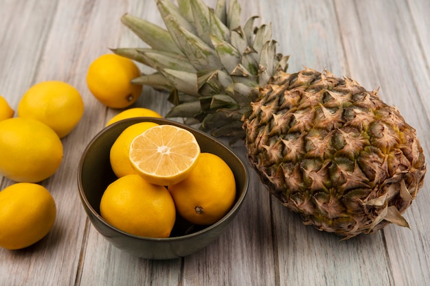 Top view of fresh lemons on a bowl with pineapple and lemons isolated on a grey wooden background