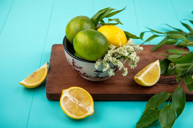 Top view of fresh lemons on bowl on wood kitchen board with leaves on blue