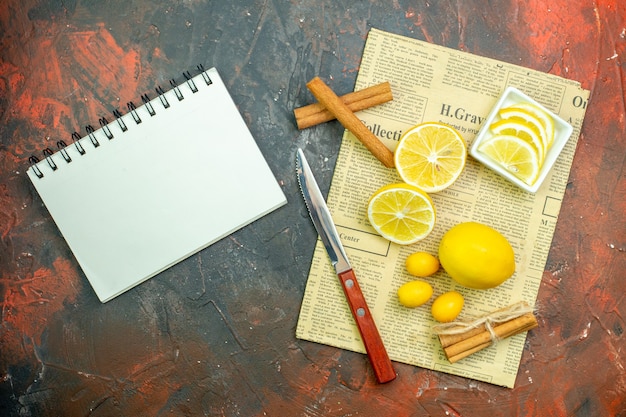 Вид сверху свежие лимоны cumcuats корицы дольки лимона в небольшой миске нож на газетной записной книжке на темно-красном столе