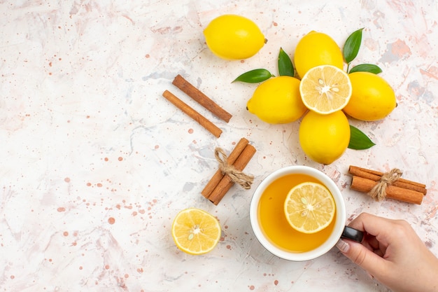 Вид сверху свежие лимоны нарезанные лимонные палочки корицы чашка чая с лимоном в руке женщины на яркой изолированной поверхности свободное пространство