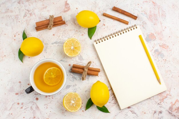 Top view fresh lemons cut lemon cinnamon sticks a cup of lemon tea notepad on bright isolated surface