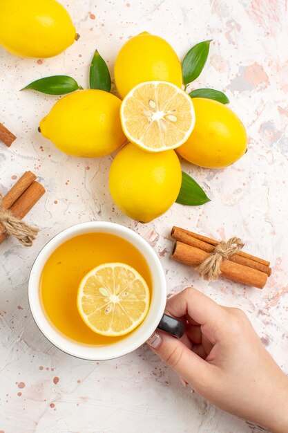 Вид сверху свежих лимонов, нарезанных лимонными палочками корицы, чашка чая с лимоном в руке женщины на яркой изолированной поверхности