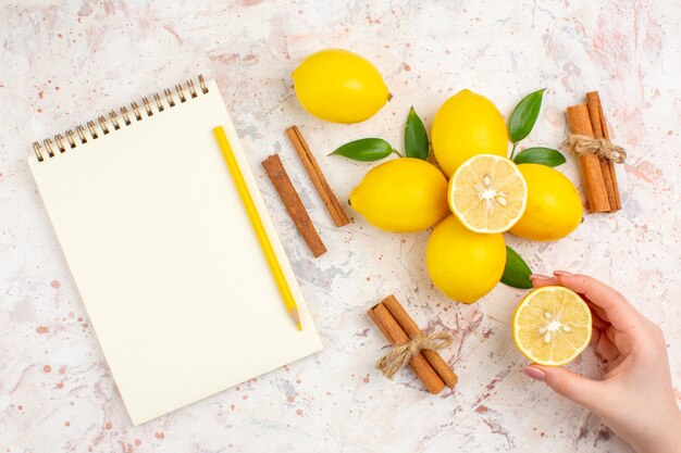 Top view fresh lemons cut lemon in female hand cinnamon sticks yellow pencil in female hand on bright isolated surface