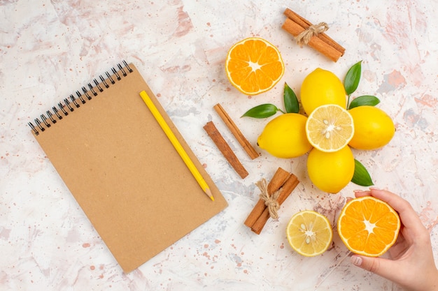 Вид сверху свежие лимоны, разрезанные апельсиновые палочки корицы, разрезанные апельсином в женской руке, карандаш для ноутбука на яркой изолированной поверхности
