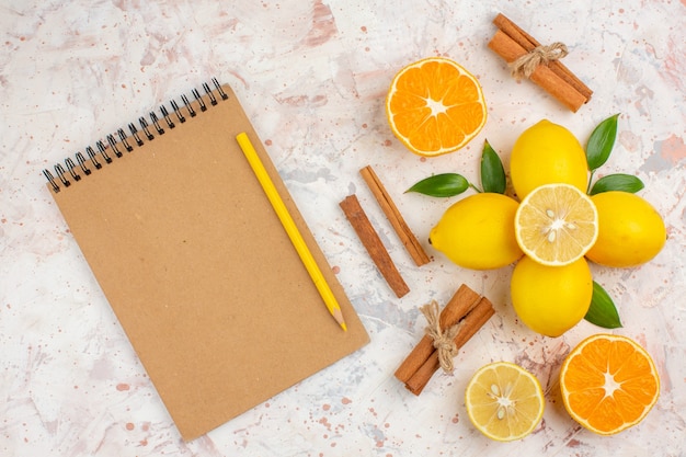 상위 뷰 신선한 레몬 잘라 오렌지 계 피 스틱 밝은 고립 된 표면에 여성 손 노트북 노란색 연필에 오렌지를 잘라