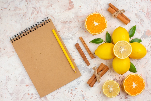 Top view fresh lemons cut orange cinnamon sticks cut orange in female hand notebook yellow pencil on bright isolated surface