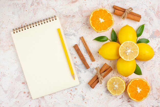 Вид сверху свежих лимонов, нарезанных оранжевыми палочками корицы, желтым карандашом на блокноте на яркой изолированной поверхности