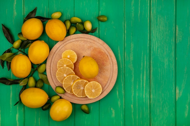 Top view of fresh lemons slices on a wooden kitchen board with kinkans and lemons isolated on a green wooden wall with copy space