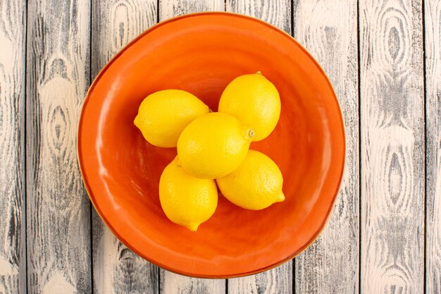 A top view fresh lemons sour ripe mellow juicy citrus inside orange plate vitamine yellow on the grey rustic desk