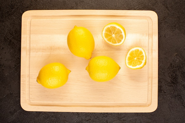 トップビューフレッシュレモンは熟した全体を酸っぱくし、暗い机の上に黄色のまろやかな柑橘系トロピカルビタミンイエローをスライス