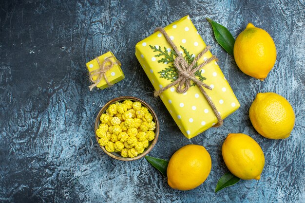 Top view of fresh lemons with leaves and yellow gift box cookies in a brown pot on dark background