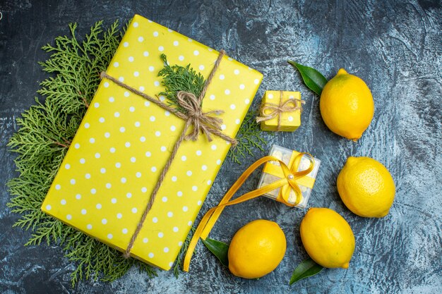 Vista dall'alto di limoni freschi con foglie e confezione regalo gialla su rami di abete su sfondo scuro