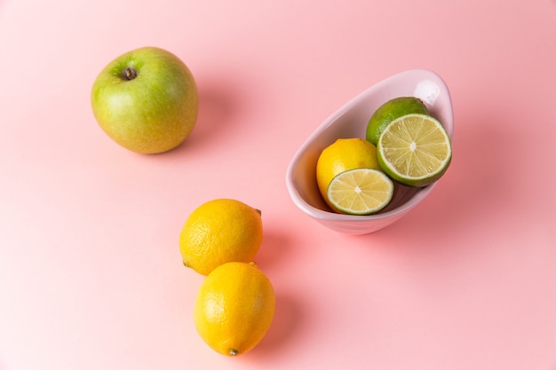 Top view of fresh lemons with sliced lime inside plate on the light-pink surface