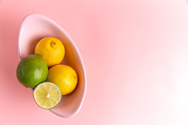 Vista dall'alto di limoni freschi con calce a fette all'interno della piastra sulla superficie rosa